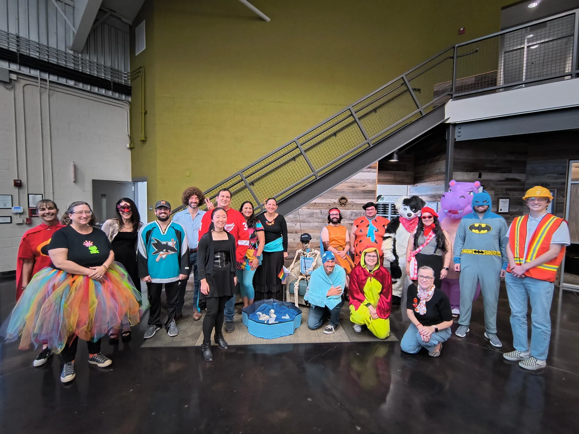 19 people dressed in costumes pose with a skeleton next to stairs in ANR building foyer