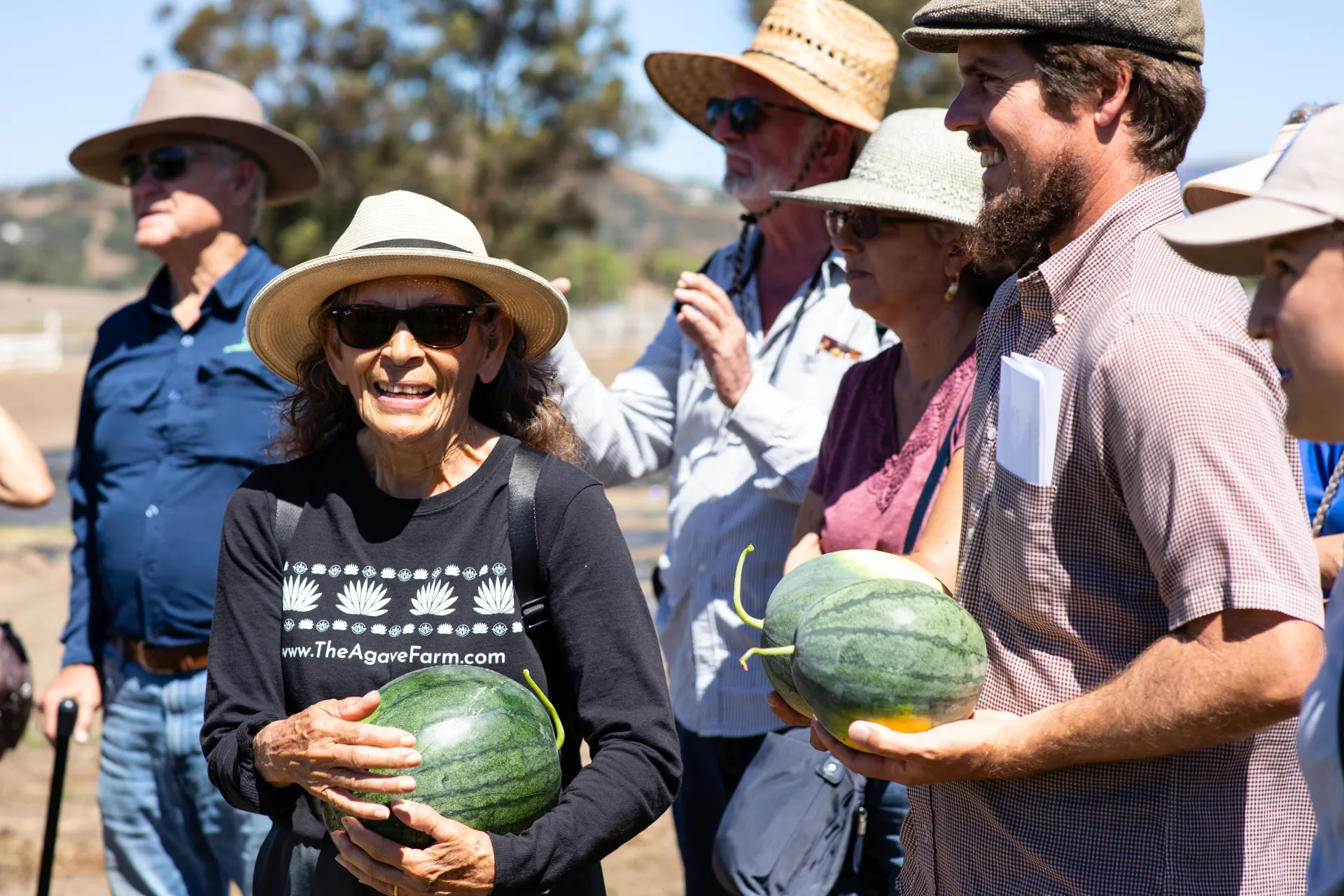 People stand outside holding watermelons