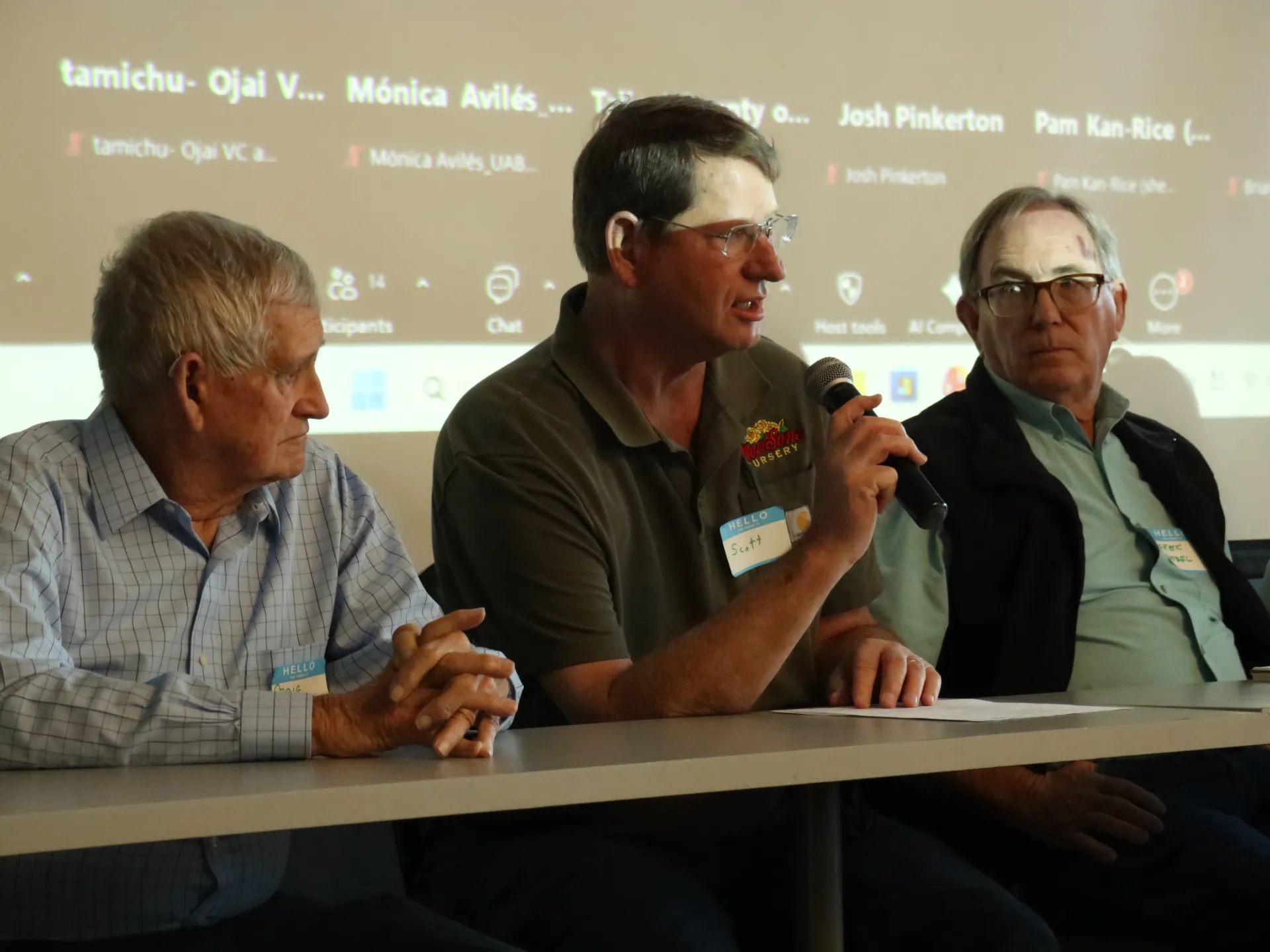 A person speaks into a microphone while two people listen on his left and right