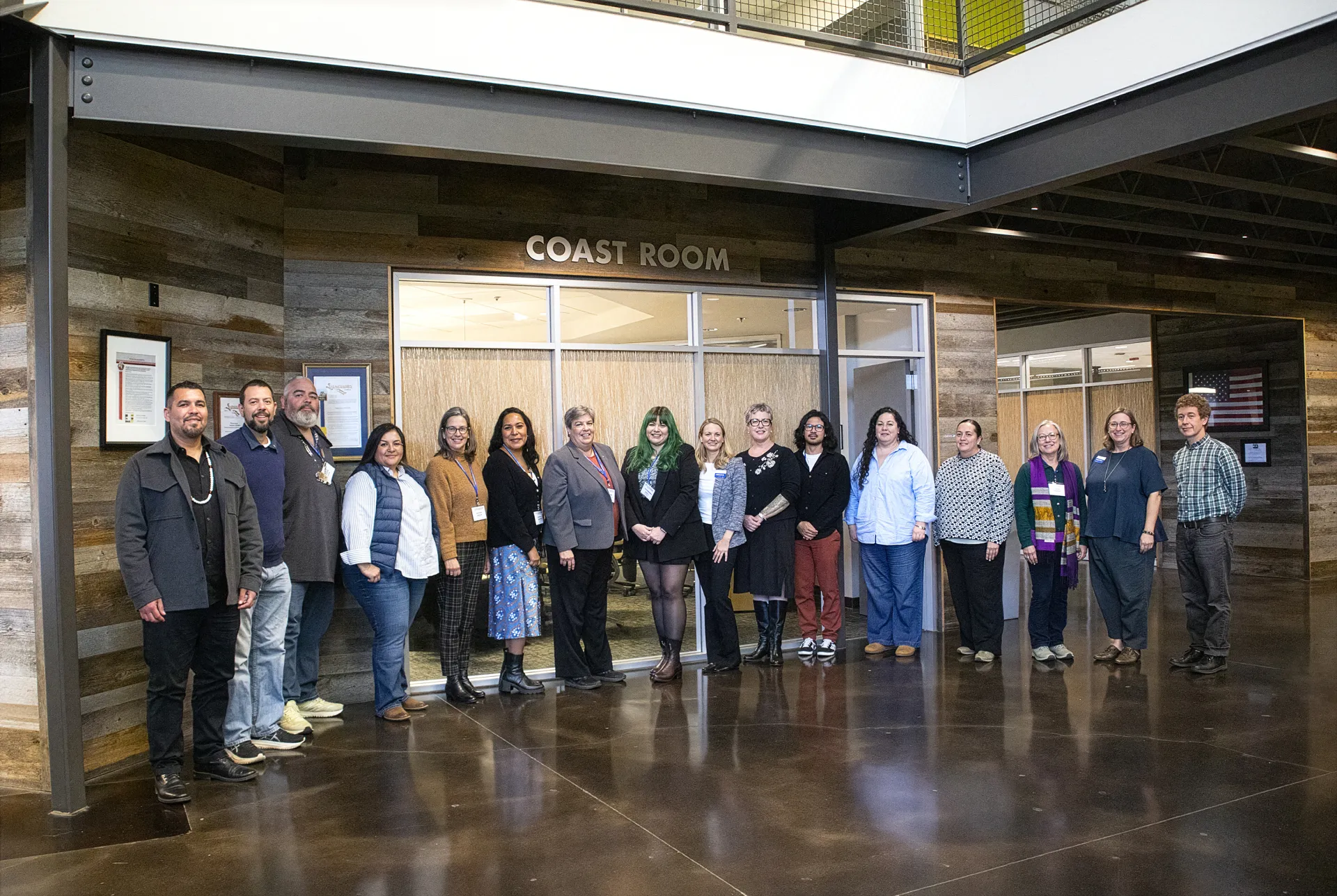 Sixteen people stand posing outside of the Coast Room
