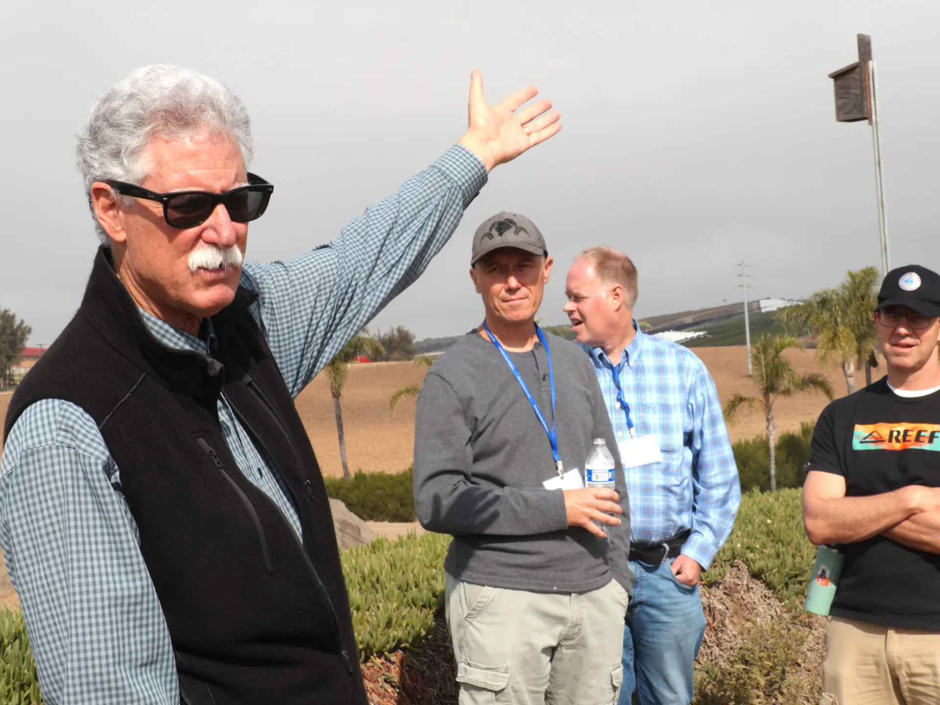 A farmer in sunglasses speaks to a tour group