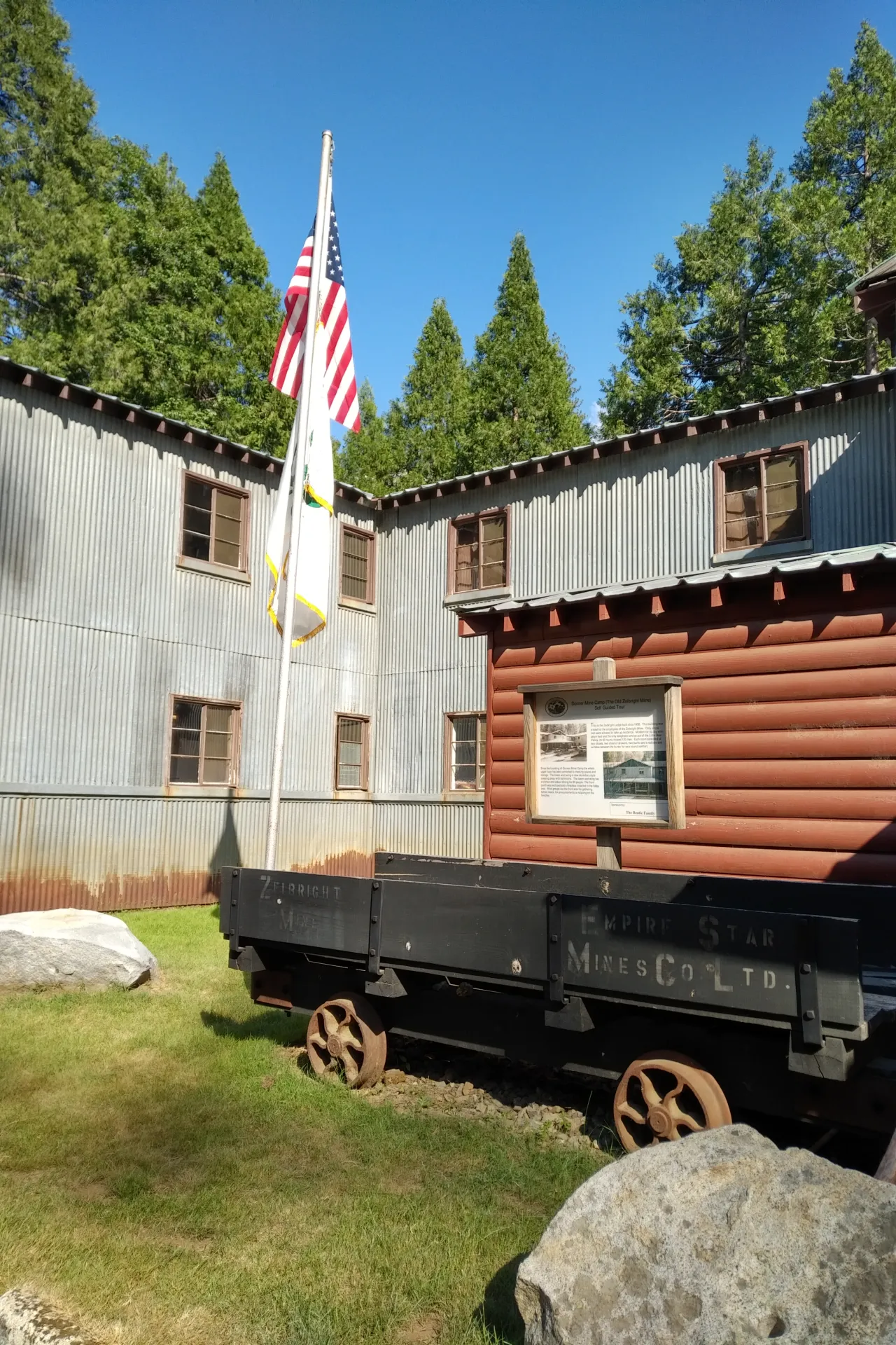 The historic camp's main building with an original mine cart and an American flag and a 4-H flag raised on a flag pole.