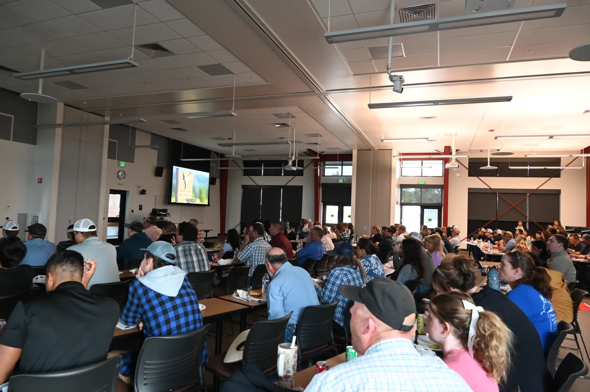 A documentary plays on a screen at the front of the room full of people sitting in rows