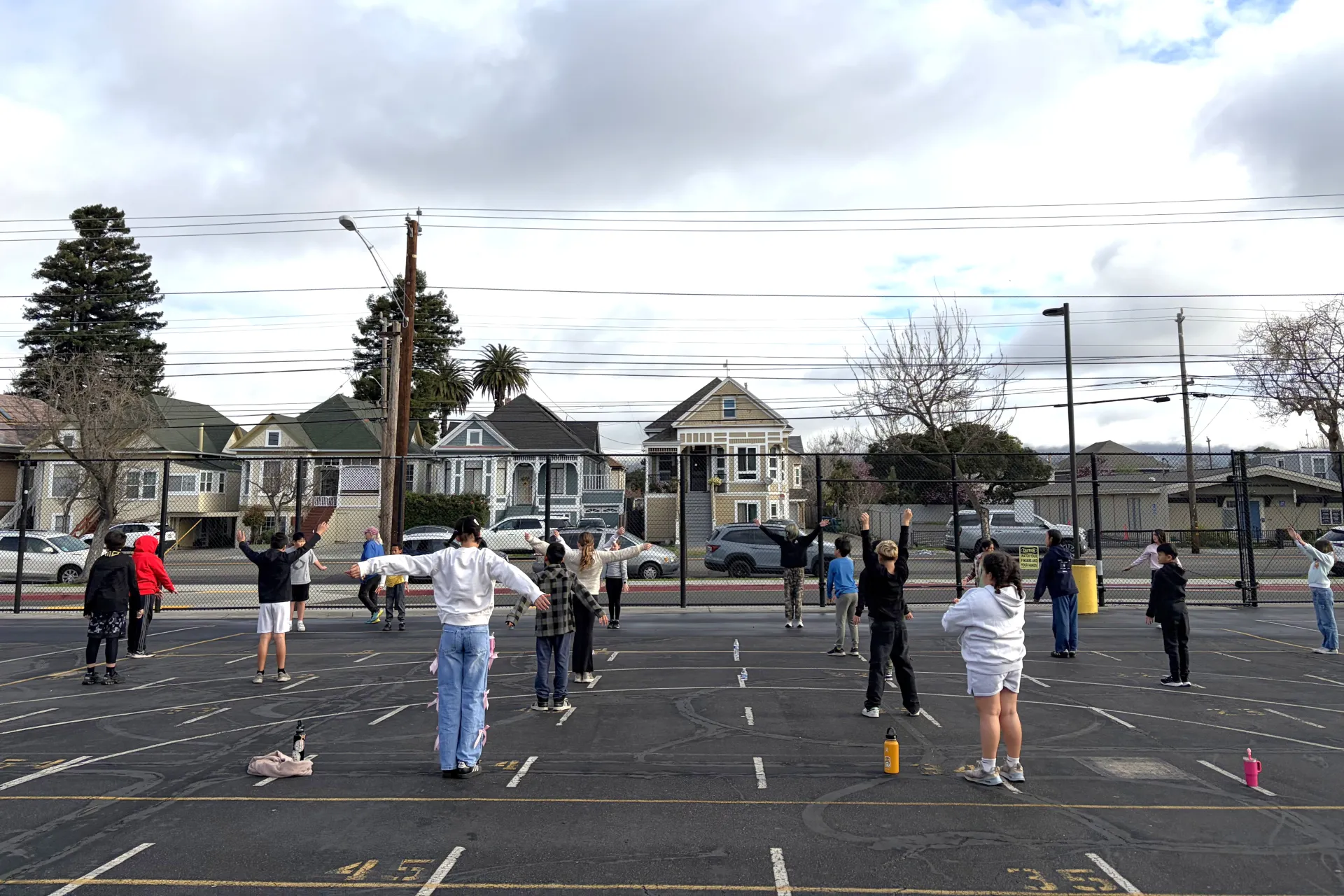 A physical education teacher leads a class of fifth graders through warmups and stretches on a school yard
