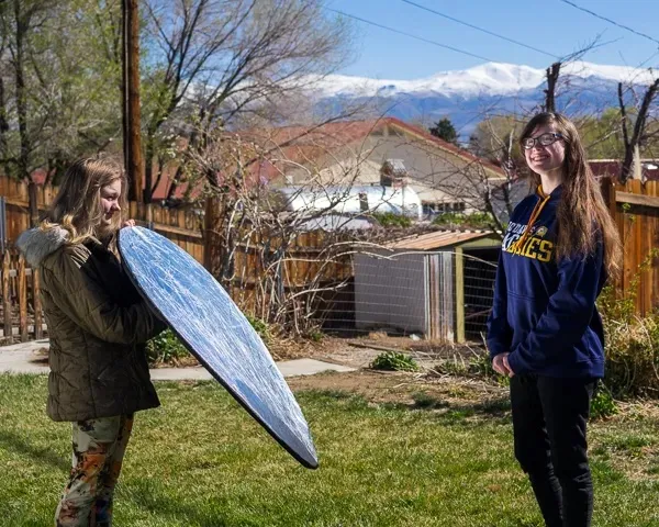 Two individuals, one holding reflector towards other