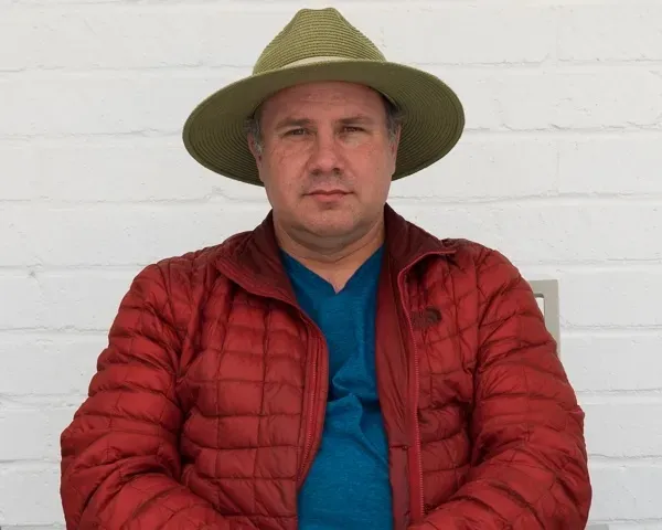 Man in red jacket sitting against white brick background, an example of very soft light shot under a shade cloth