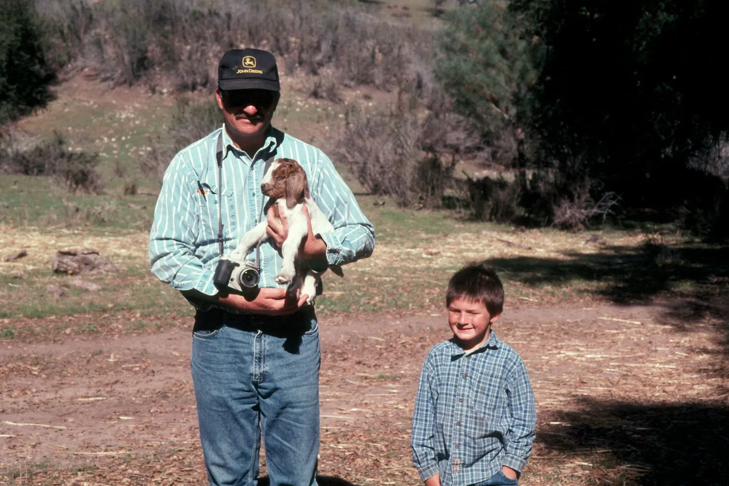 Royce Larsen holding a kid goat stands next to a child