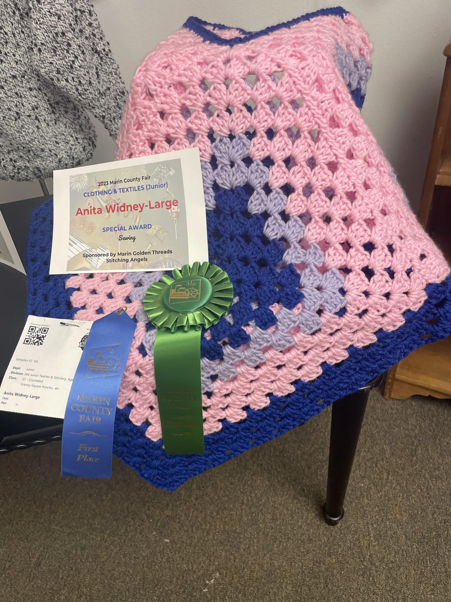 A hand-crocheted pink, purple, and blue granny square poncho is displayed with a Marin County Fair First Place ribbon and a Special Award ribbon.