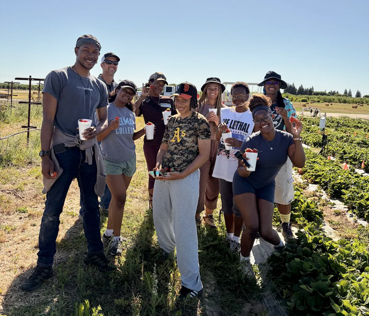 Nine people pose with strawberries in strawberry field