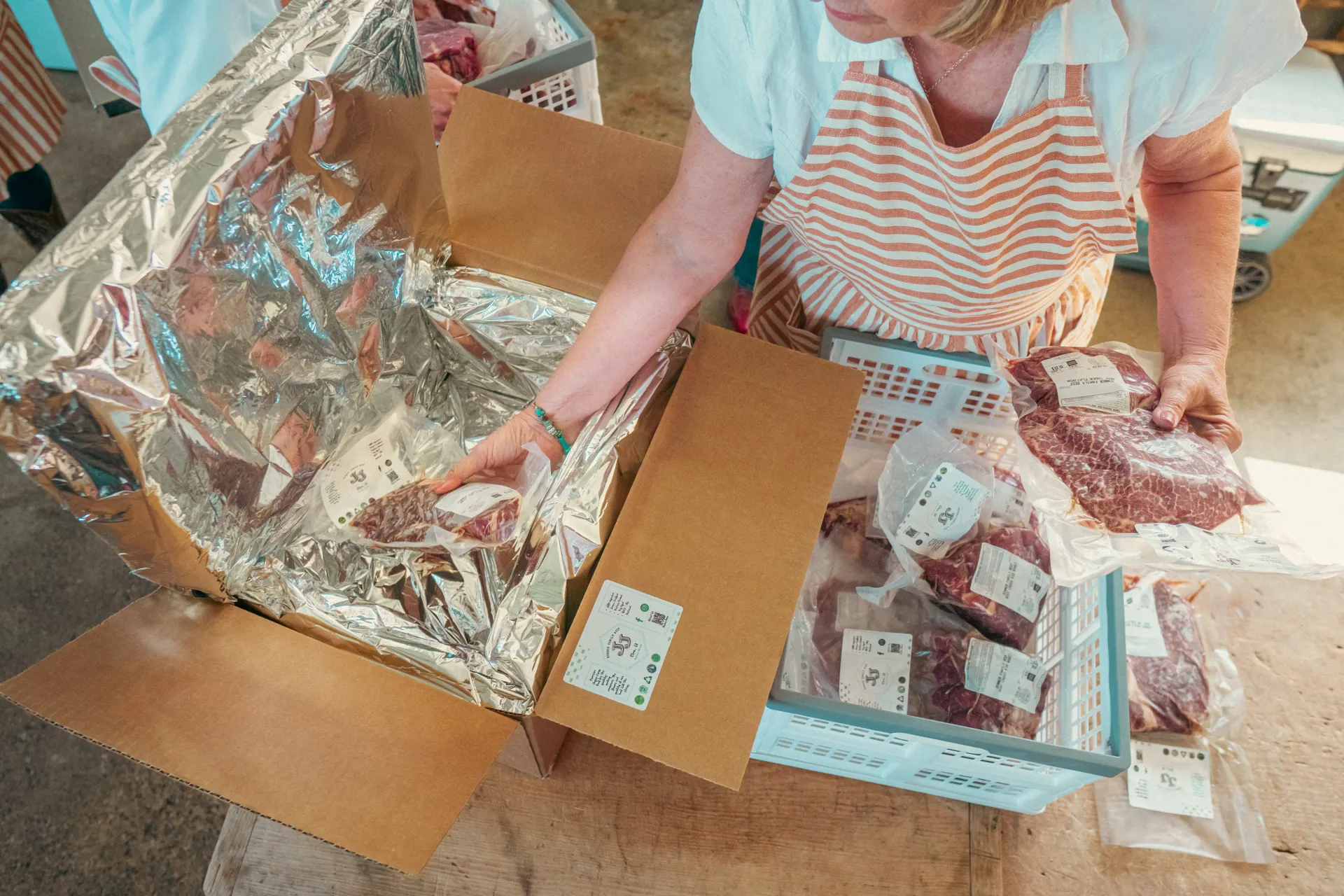 A person wearing an apron places vacuum-packed beef into a lined cardboard shipping box.