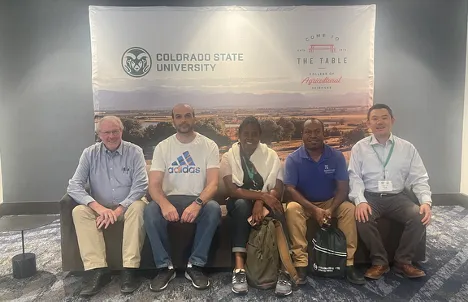 Five people sit on a bench in front of a Colorado State University banner