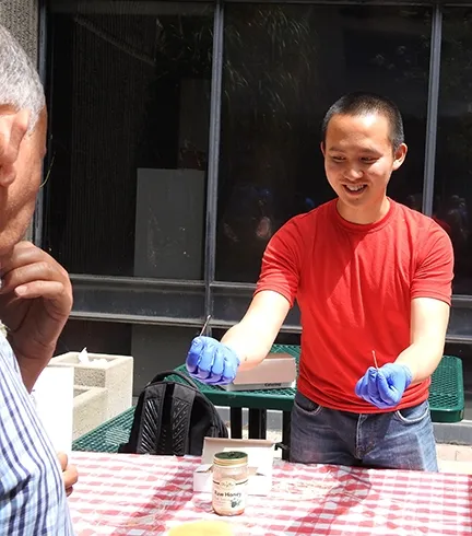 Graduate student Yao Cai of the Joanna Chiu lab holds a honey-coated toothpick in each hand. (Photo by Kathy Keatley Garvey)