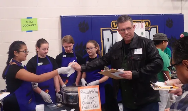 Vacaville police officer Shawn Windham, president of the Vacaville Unified School District Board of Trustees, prepares to evaluate the chili of the Pleasants Valley 4-H team (from left) Maliyah Desmarais, Maya Farris, Naomi Lipary and Jessie Means. (Photo by Kathy Keatley Garvey)