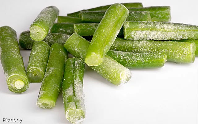 Frozen green beans stacked on a white background, showing a light frost coating on each bean.