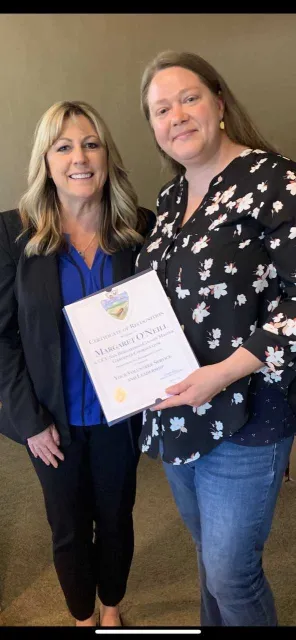 Maggie receiving recognition from Supervisor Rowe's Chief of Staff Gayle Covey