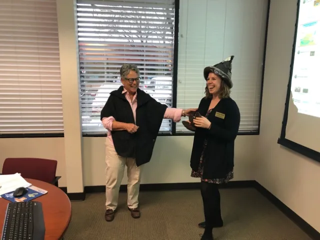 Two women, one touching arm of course instructor who is wearing a poop emoji hat.