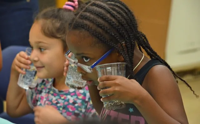Young scientist using the sense of hearing to listen to soda bubble during a Kitchen Science YES Project lesson.