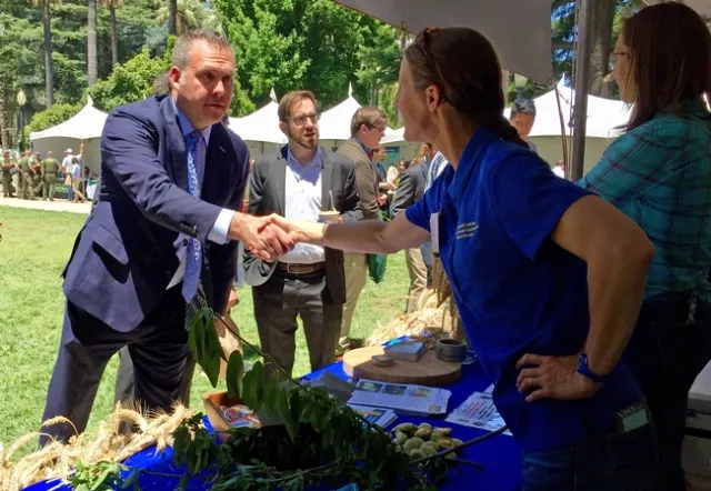 Assemblyman Gray, on left in navy-colored suit, shakes the hand of Michelle Leinfelder-Miles, who is wearing a blue ANR polo shirt.