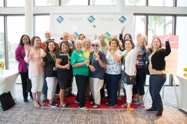 UC Master Gardener volunteers in front of a step and repeat, posing for a photograph with their hands in the air.
