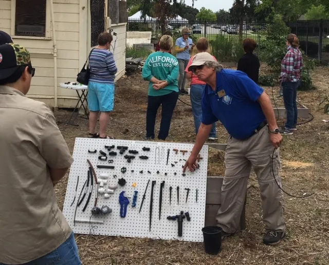 Harry Lee wearing a blue MG polo shirt pointing to an item on his homeade display board with stakes, tubes and valves.