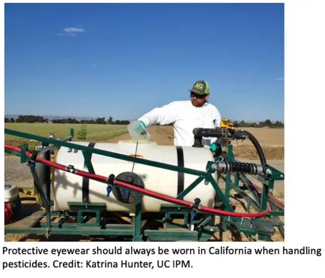 Person wearing protective eyewear, gloves, coveralls, and hat while handling and pouring pesticide into tank.