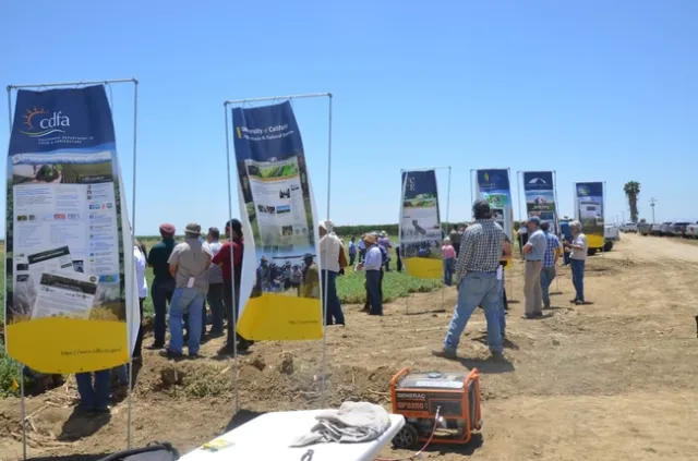 Farmers and Cooperative Extension academics are talking in small groups and reading informational signs.