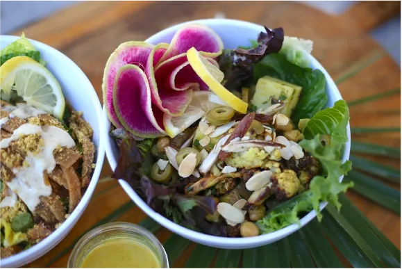 A white bowl containing artfully arranged vegetables and nuts atop a bed of lettuce.