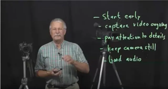 Jeff Mitchell stands next to a camera on a tripod, holding a mic. Next to him it says, 