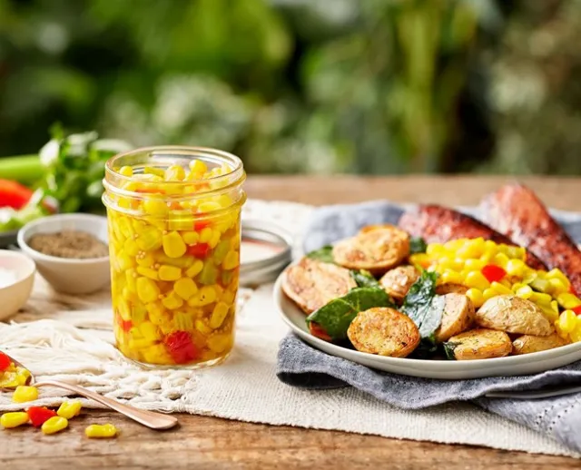 Jar of corn relish and on a plate with other food