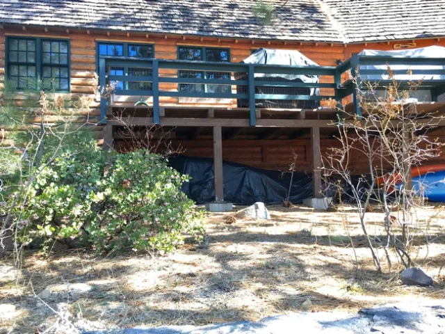 Kayaks and large items under black plastic tarps stored beneath a deck.