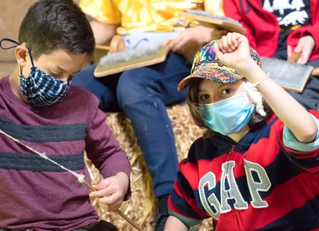 Boy on left twists the wool into yarn while a boy on the right shows the yarn bracelet on his wrist.