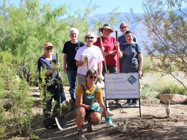 A group of people standing near a sign in a garden.