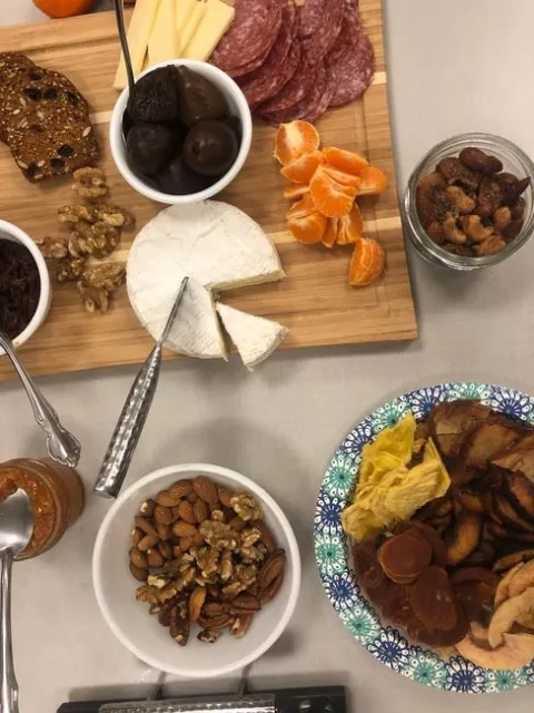 Mixed nuts in bowls shown with a wheel of brie, mandarin segments, salami and dried fruit.