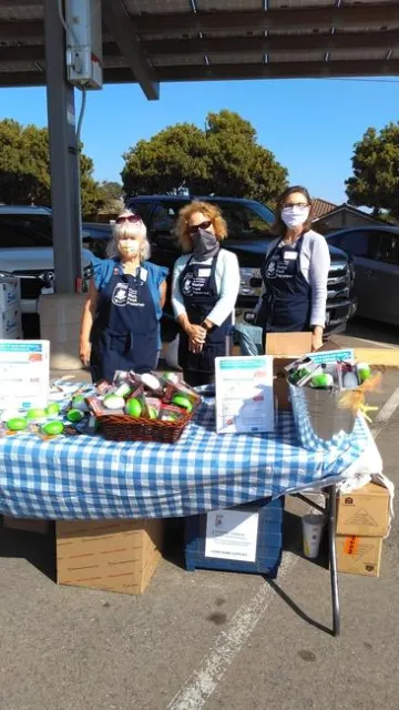 Three people with blue aprons in a parking lot standing in front of a table with information and materials