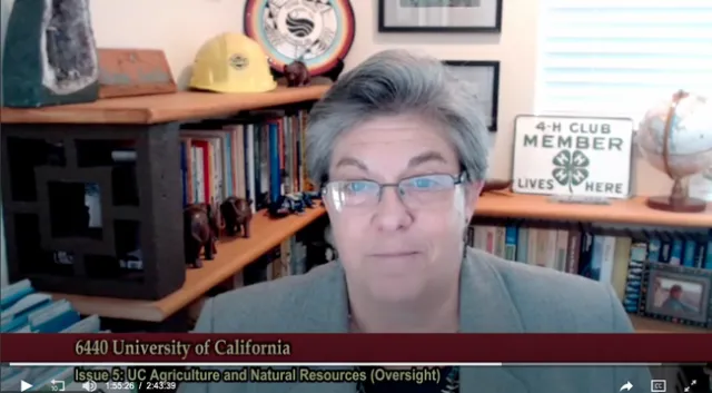 Glenda Humiston speaks onscreen. A plaque on the bookshelf behind her reads, 