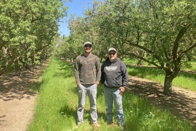 Rob Schuh and son-in-law Andrew Carroll standing in their almond orchard. Photo by Caddie Bergren.