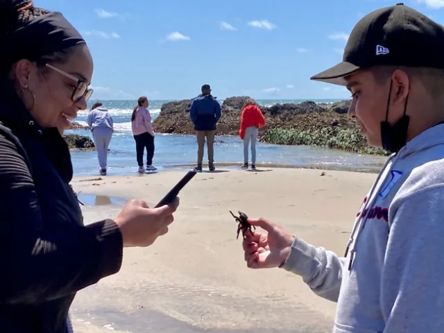 A chaperone takes a photo of a crab held by a boy.