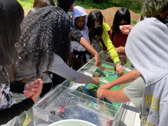 Students place clay walls and dams onto the landscape to guide water around houses.