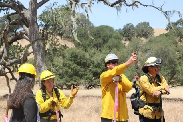 Woman wearing a hard hat listens to a woman wearing fire fighting gear.