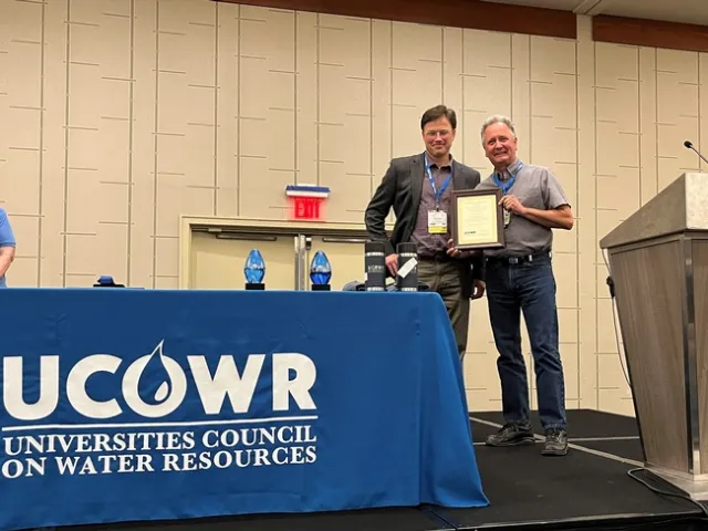 Two men standing on stage with plaque.