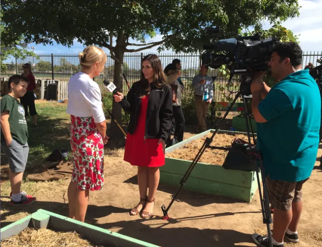 Feenstra speaks into mic held by a female reporter as a videographer records.