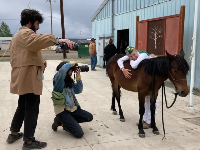 Kailey rests her arms on the horse's back as she smiles, looking at the horse's face.