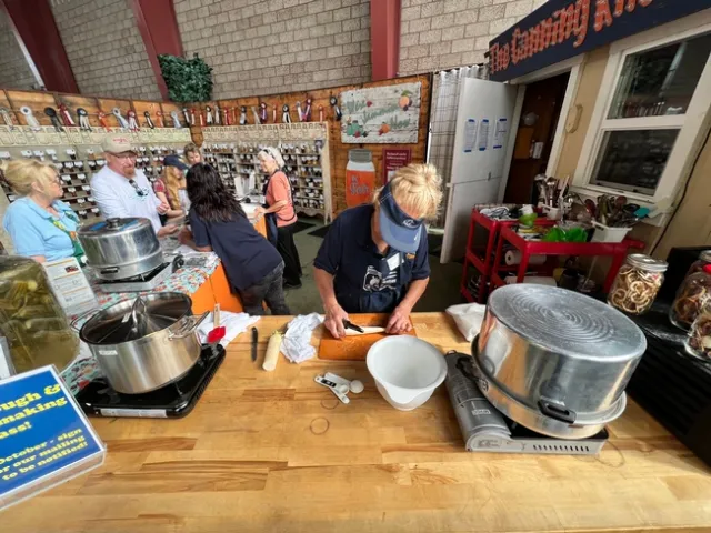 Farm-house themed booth with two volunteers speaking to visitors and third volunteer cutting vegetables.