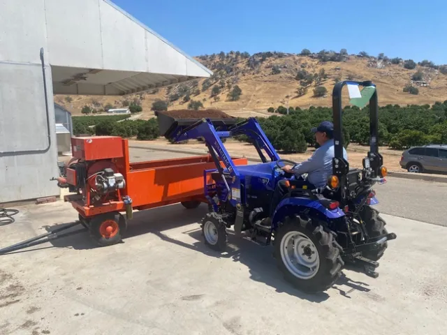 A blue tractor dumps soil into an orange bin for mixing.