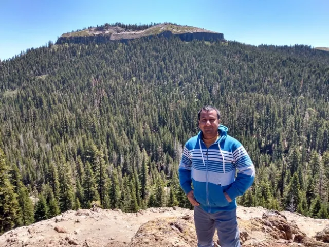 Khan smiles from a cliff with acres of forest stretch out behind him.
