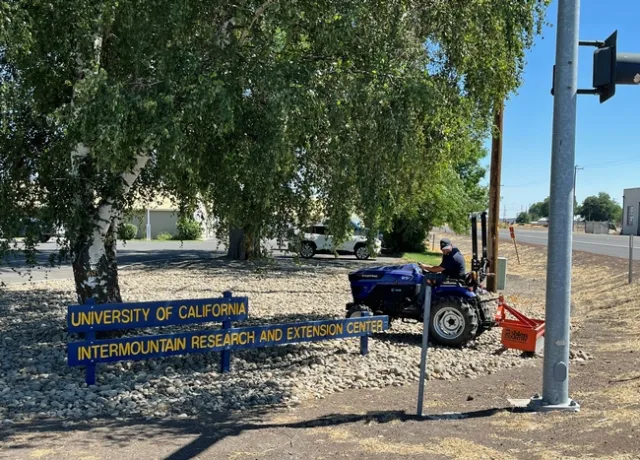 A tractor maneuvers around the IREC sign and trees.