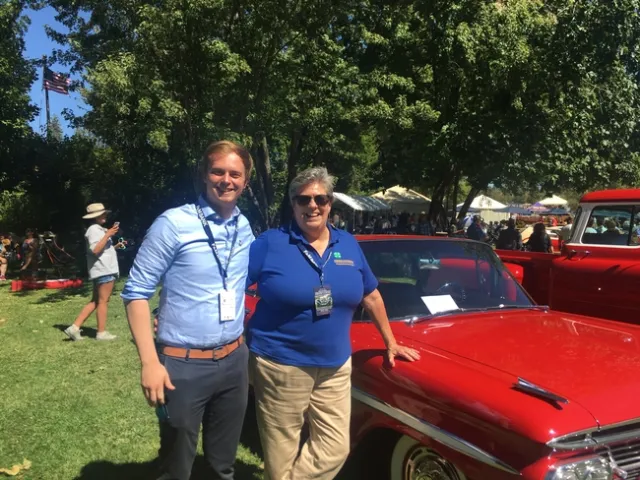 Brandon and Humiston pose beside a shiny, cherry red classic car.