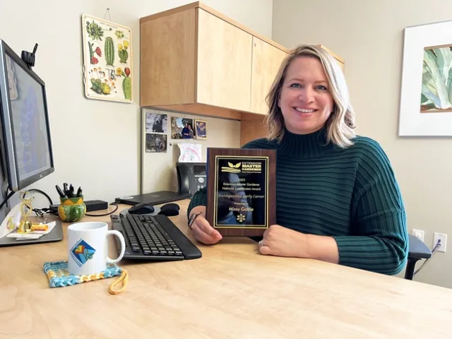 Missy at in her office holding up her award plaque.