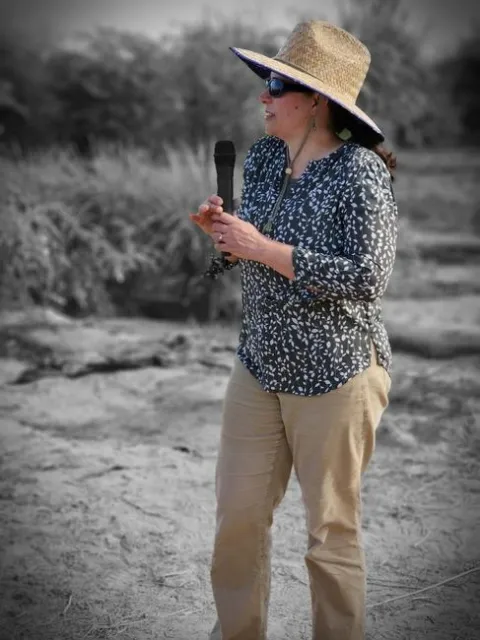 Ruth stands in field holding a mic
