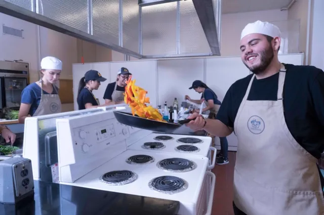 A student in the Cal Teaching Kitchen sautes bell peppers in a frying pan